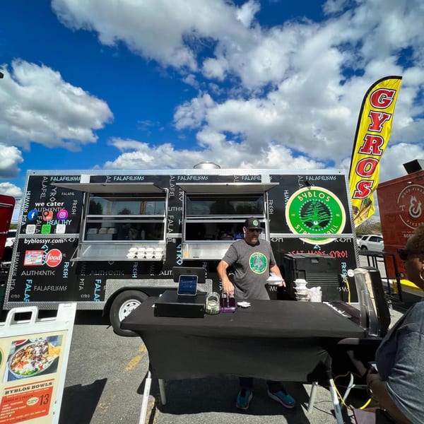 A Byblos Mediterranean Cafe food truck with a vendor serving a customer under a blue sky.