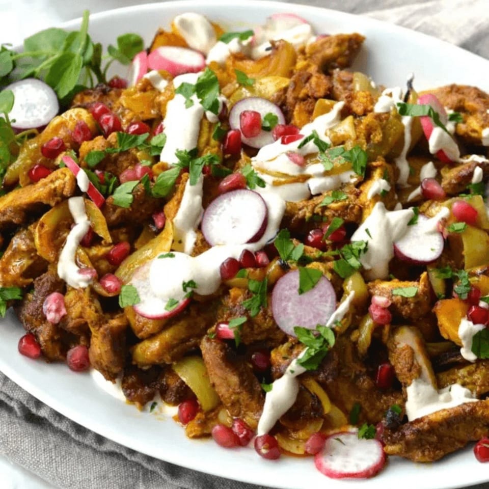 Middle Eastern platter of roasted vegetables and falafel topped with yogurt sauce, radishes, pomegranate seeds, and herbs.