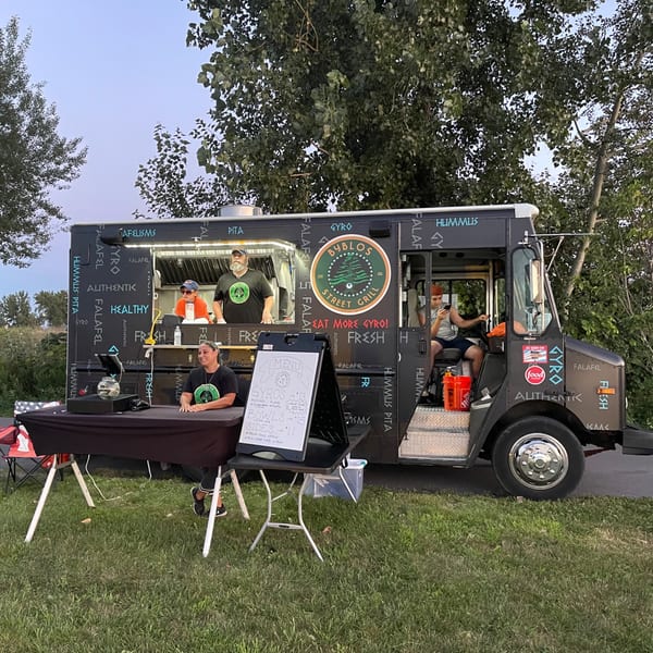 Byblos Mediterranean Cafe food truck with three staff members, a menu board, and a table setup outdoors.