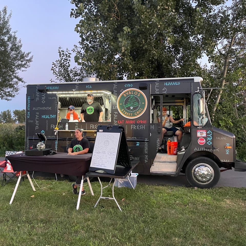 Byblos Mediterranean Cafe food truck with three staff members, a menu board, and a table setup outdoors.