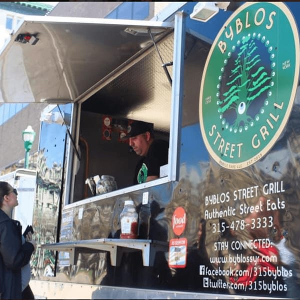 A customer orders from the Byblos Street Grill food truck, featuring its logo and contact information.