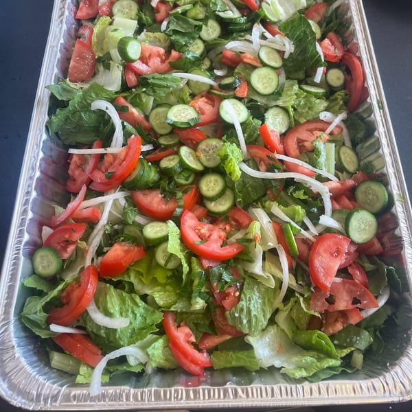 A large aluminum tray filled with a fresh salad of lettuce, sliced tomatoes, cucumbers, and onions.
