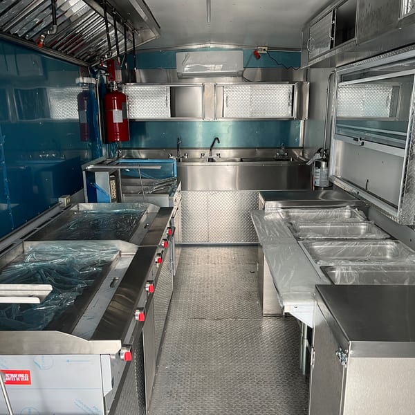 Interior of a new, empty food truck kitchen with stainless steel surfaces and blue walls.