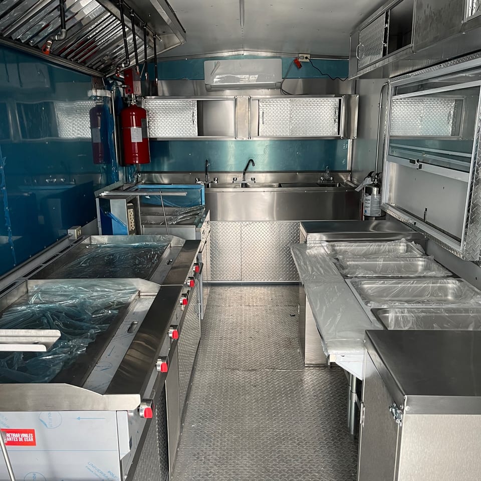 Interior of a new, empty food truck kitchen with stainless steel surfaces and blue walls.