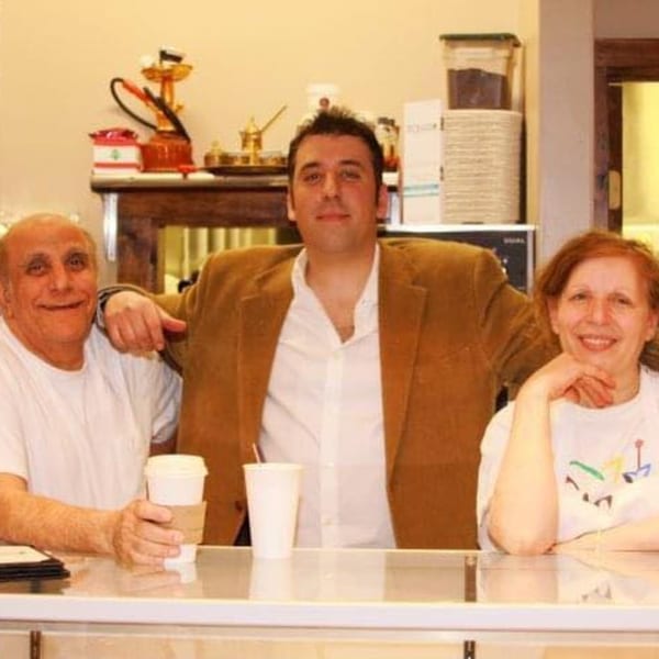 Three smiling Byblos Mediterranean Cafe staff members, two men and one woman, behind a counter.
