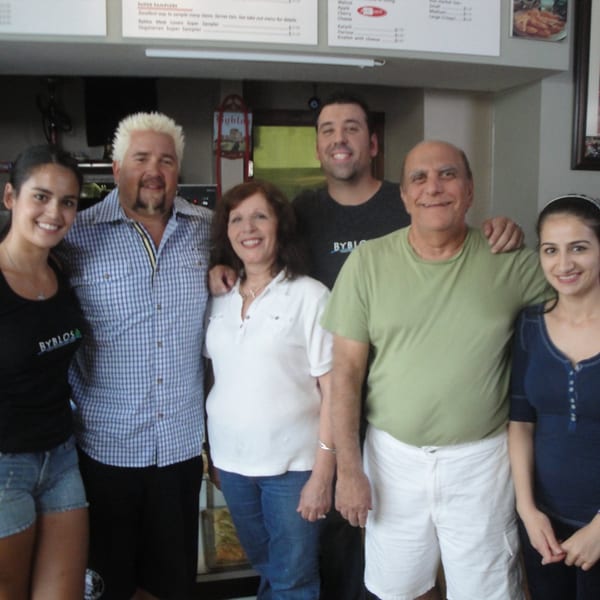 Guy Fieri and the Byblos Mediterranean Cafe staff smiling together inside the restaurant.