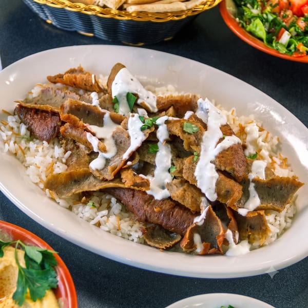 Delicious gyro meat and rice dish, drizzled with white sauce and fresh parsley.