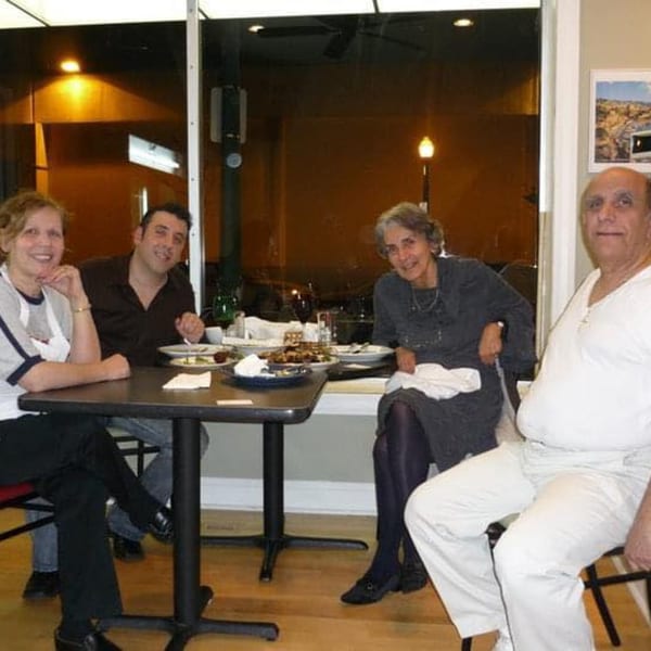 Four people, two men and two women, smiling while seated around a table with food at Byblos Mediterranean Cafe.
