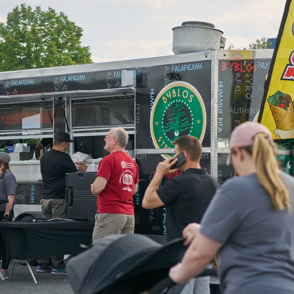 People gather around the Byblos Mediterranean Cafe food truck, featuring its logo and menu items.