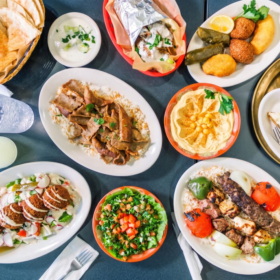Overhead view of a table laden with various Middle Eastern dishes including kebabs, falafel, hummus, and shawarma.