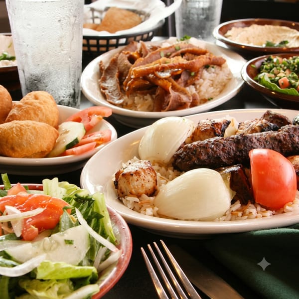 A table filled with various Middle Eastern dishes including kebabs, shawarma, rice, salads, and fried dough.