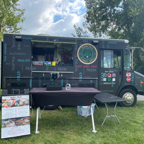 Byblos Mediterranean Cafe's black food truck with a menu board and tables set up outdoors.